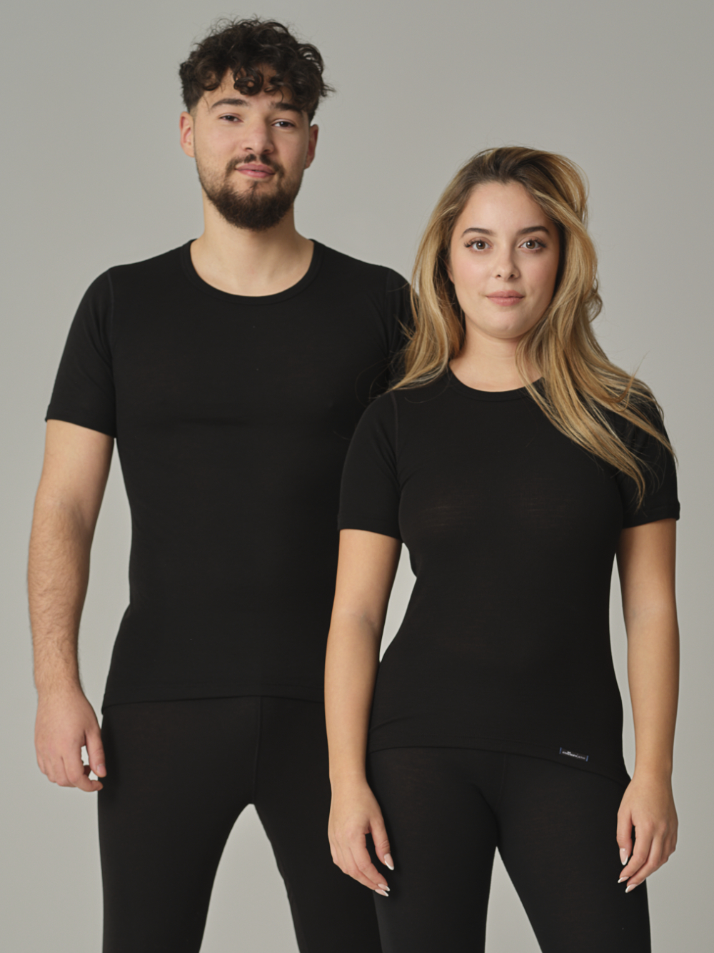 Vorderansicht: Eine Frau und ein Mann tragen Unisex Funktionsshirt "warm extra" kurzarm von Comazo in der Farbe Schwarz mit angerauter Innenseite zur optimalen Wärmespeicherung, Feuchtigkeitsmanagement und verlängertem Rückenteil
