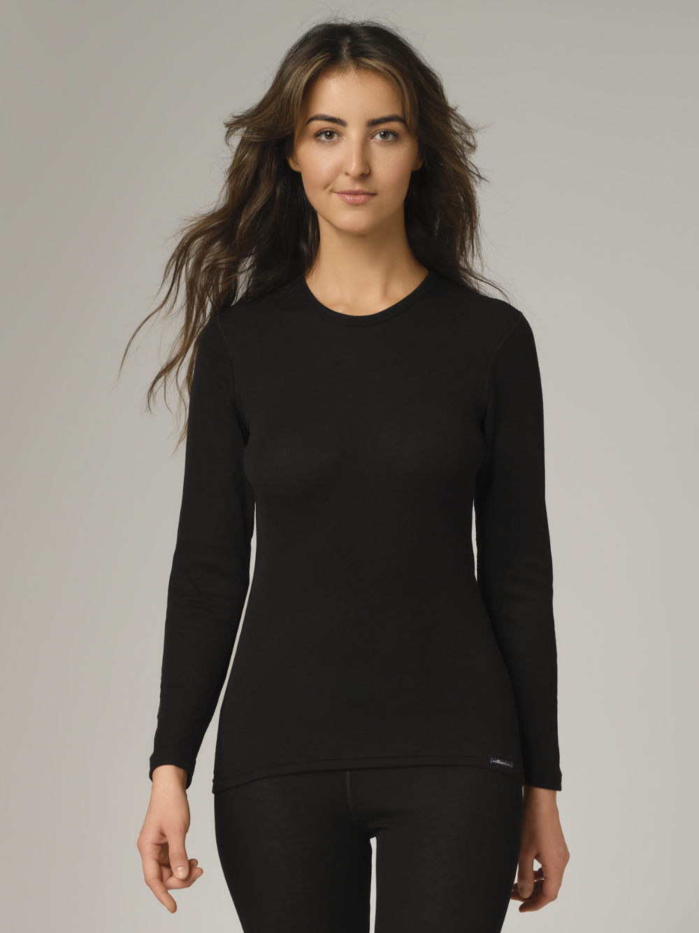 Comazo Unisex Funktionsshirt "warm extra" langarm Farbe Schwarz Vorderansicht: Frau trägt  Unisex Funktionsshirt "warm extra" langarm von Comazo in der Farbe Schwarz mit angerauter Innenseite zur optimalen Wärmespeicherung, Feuchtigkeitsmanagement und verlängertem Rückenteil