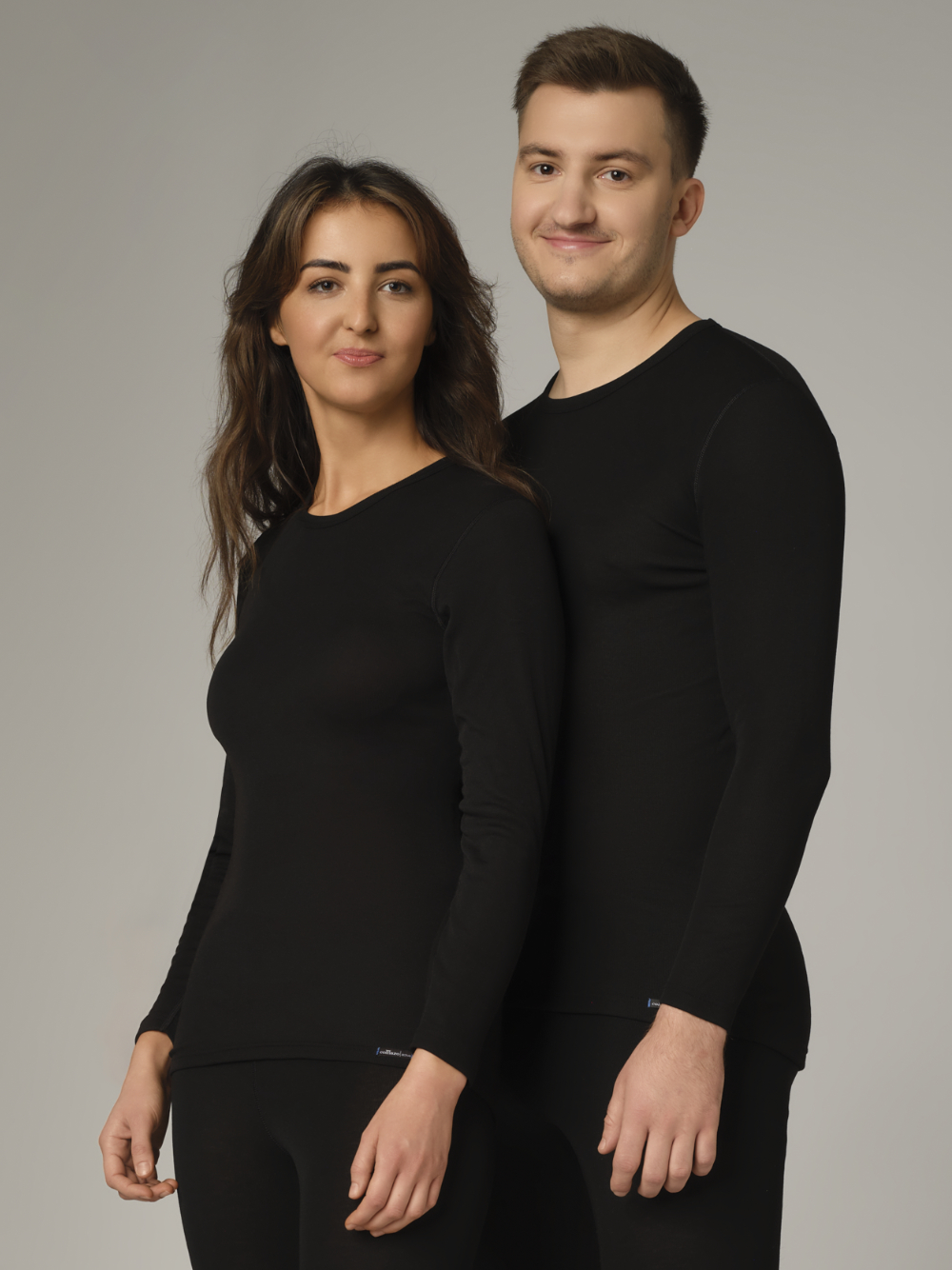 Comazo Unisex Funktionsshirt "warm extra" langarm Farbe Schwarz Vorderansicht: Eine Frau und ein Mann tragen Unisex Funktionsshirt "warm extra" langarm von Comazo in der Farbe Schwarz mit angerauter Innenseite zur optimalen Wärmespeicherung, Feuchtigkeitsmanagement und verlängertem Rückenteil