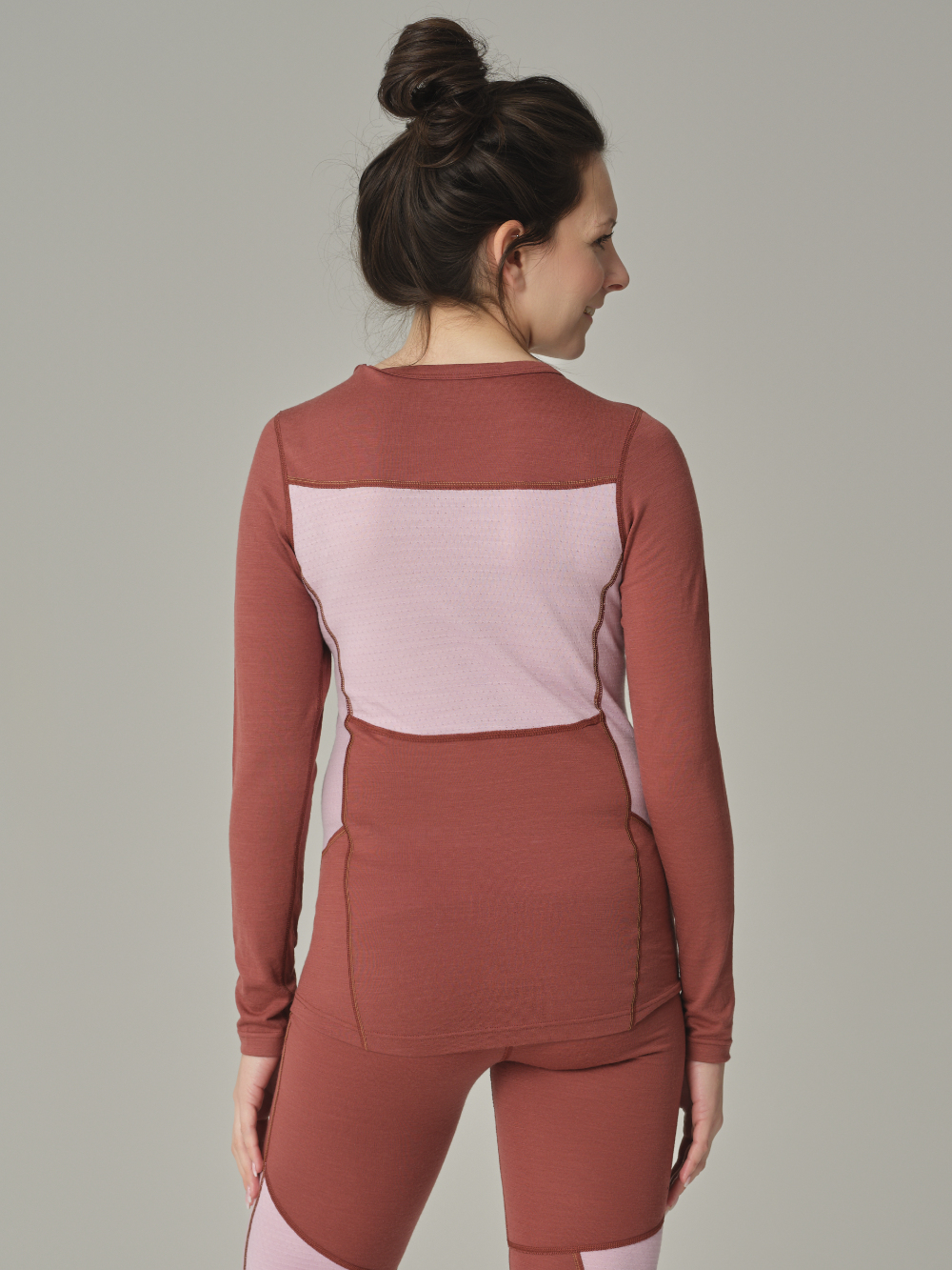 Rückansicht: Frau trägt Merinowolle-Shirt langarm von Comazo in der Farbe Brandy/Rosegrey aus 100% mulesing-freier Schurwolle mit Mesh-Einsätzen