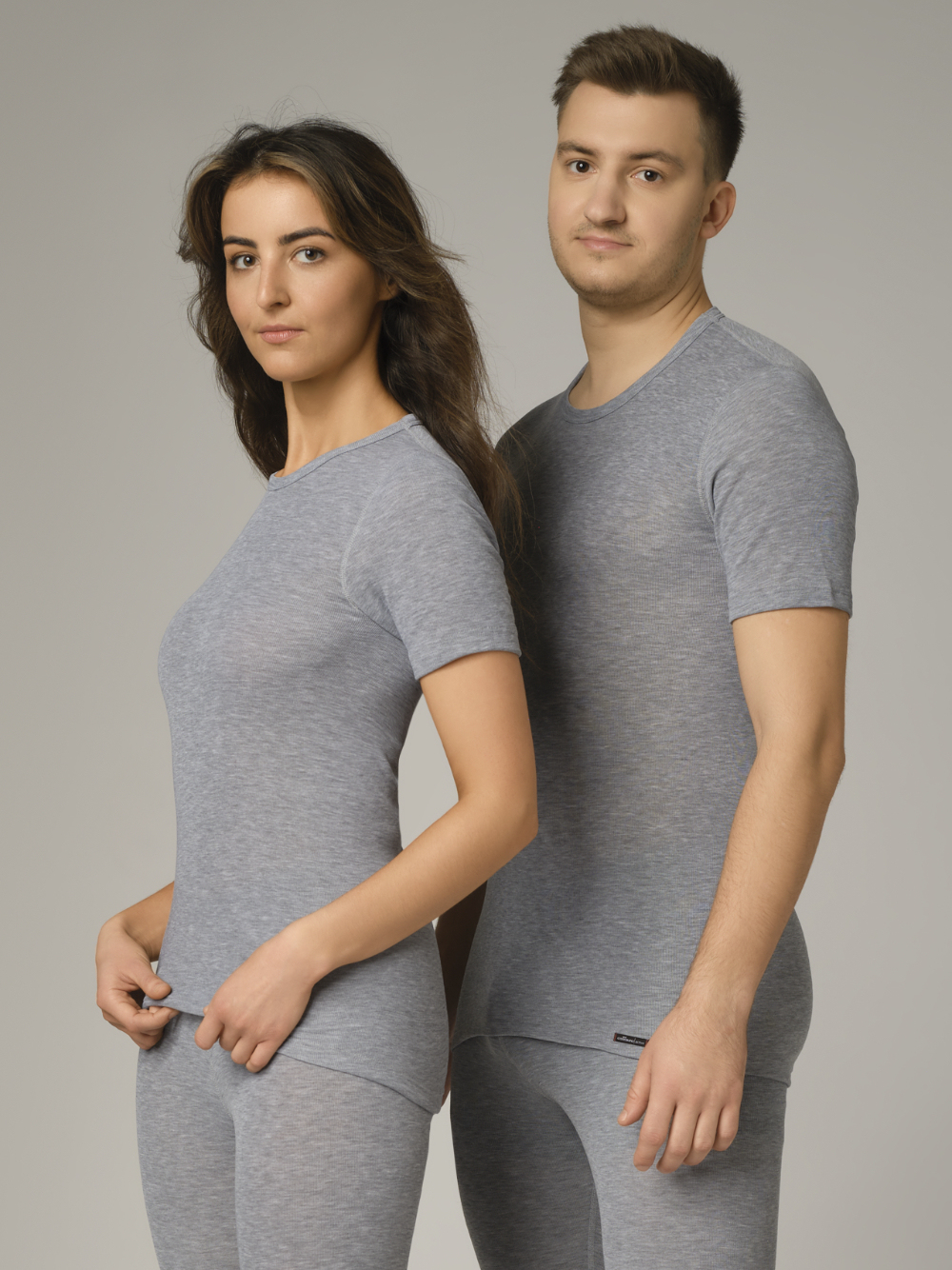 Comazo unisex short-sleeve functional shirt "warm extra", color gray melange. Front view: A woman and a man wearing unisex short-sleeve functional shirt "warm extra" by Comazo in gray melange, with a brushed inner lining for optimal heat retention, moisture management, and an extended back panel.