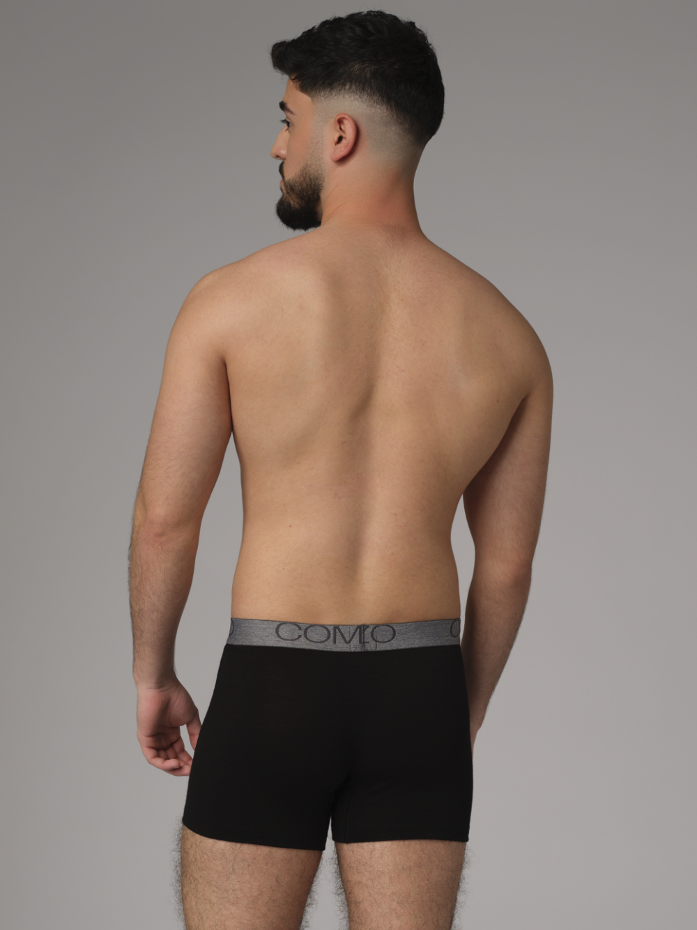 Comazo men's trunks made of merino wool in the color black. Back view: Man wearing merino wool trunks from Comazo in the color black with lettering on the waistband.