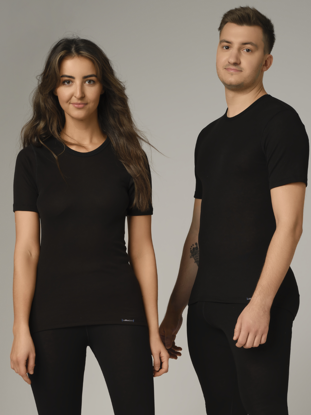 Comazo unisex short-sleeve functional shirt "warm extra", color black. Front view: A woman and a man wearing unisex short-sleeve functional shirt "warm extra" by Comazo in black, with a brushed inner lining for optimal heat retention, moisture management, and an extended back panel.