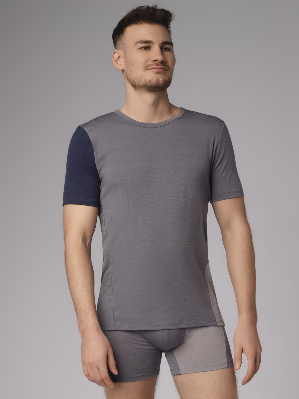 Comazo Herren Shirt kurzarm aus Merinowolle Farbe Grau/Navy Vorderansicht: Mann trägt Shirt kurzarm aus Merinowolle von Comazo in der Farbe Gray/Navy mit längerem Rückenteil und Rundhalsausschnitt