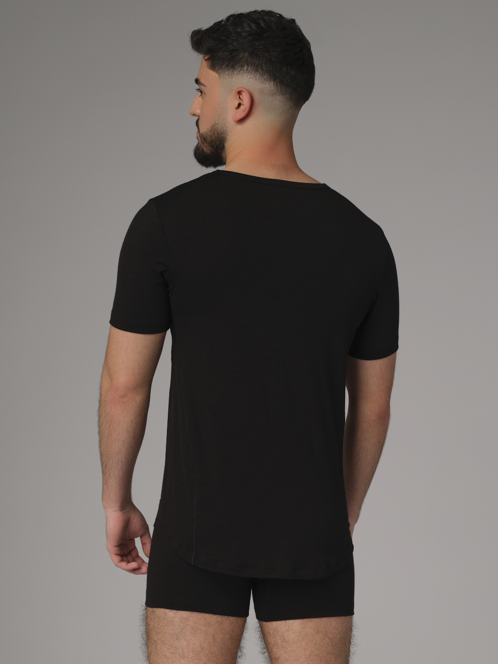 Comazo men's short-sleeve shirt made of merino wool, color black. Back view: Man wearing a short-sleeve shirt made of merino wool by Comazo in black color with extended back panel and crew neck.