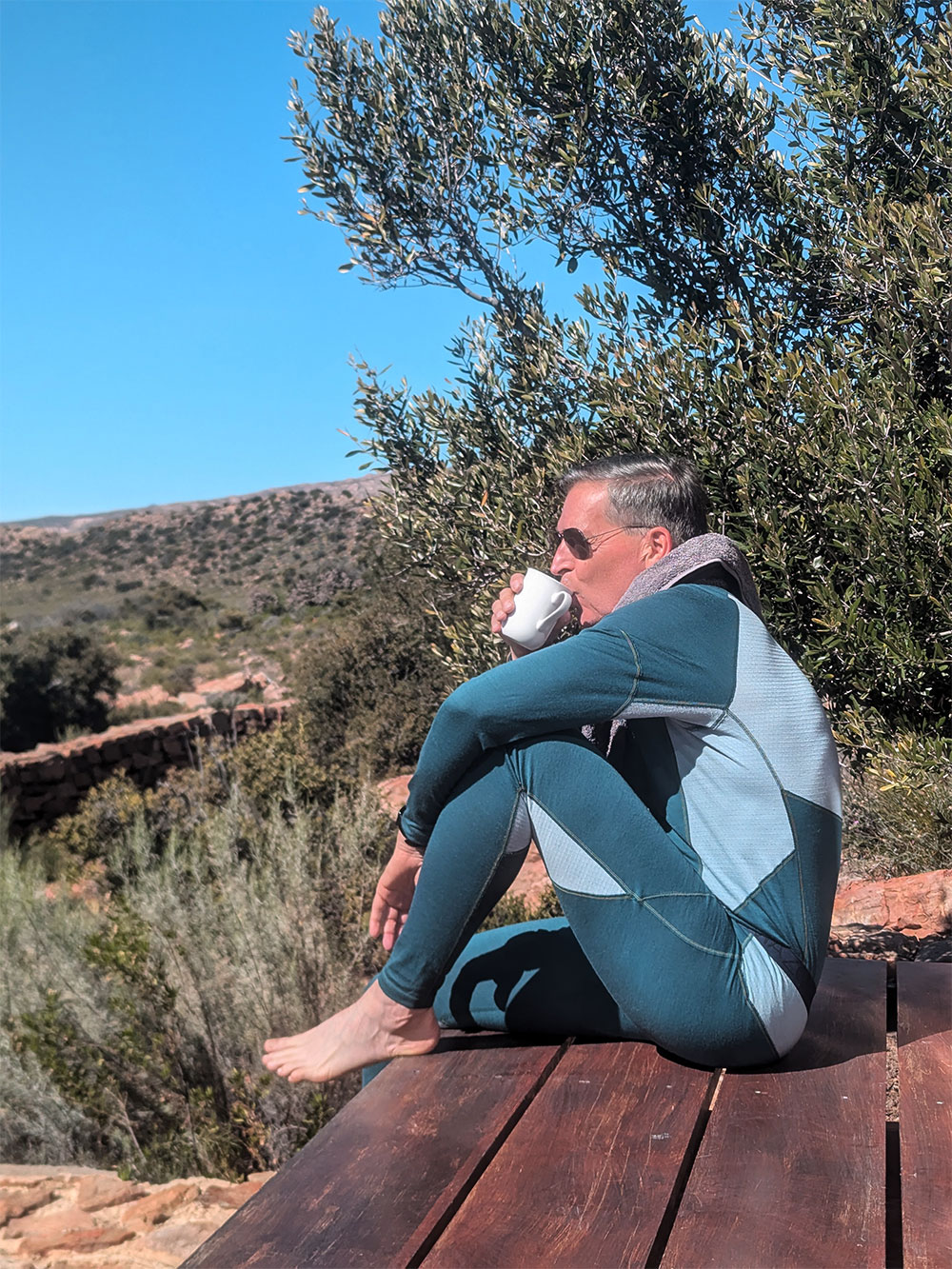 Comazo men's long underpants made of merino wool, color emerald/light green. Man sitting in nature, wearing long underpants made of 100% mulesing-free merino wool by Comazo in emerald/light green color with Comazo logo waistband.
