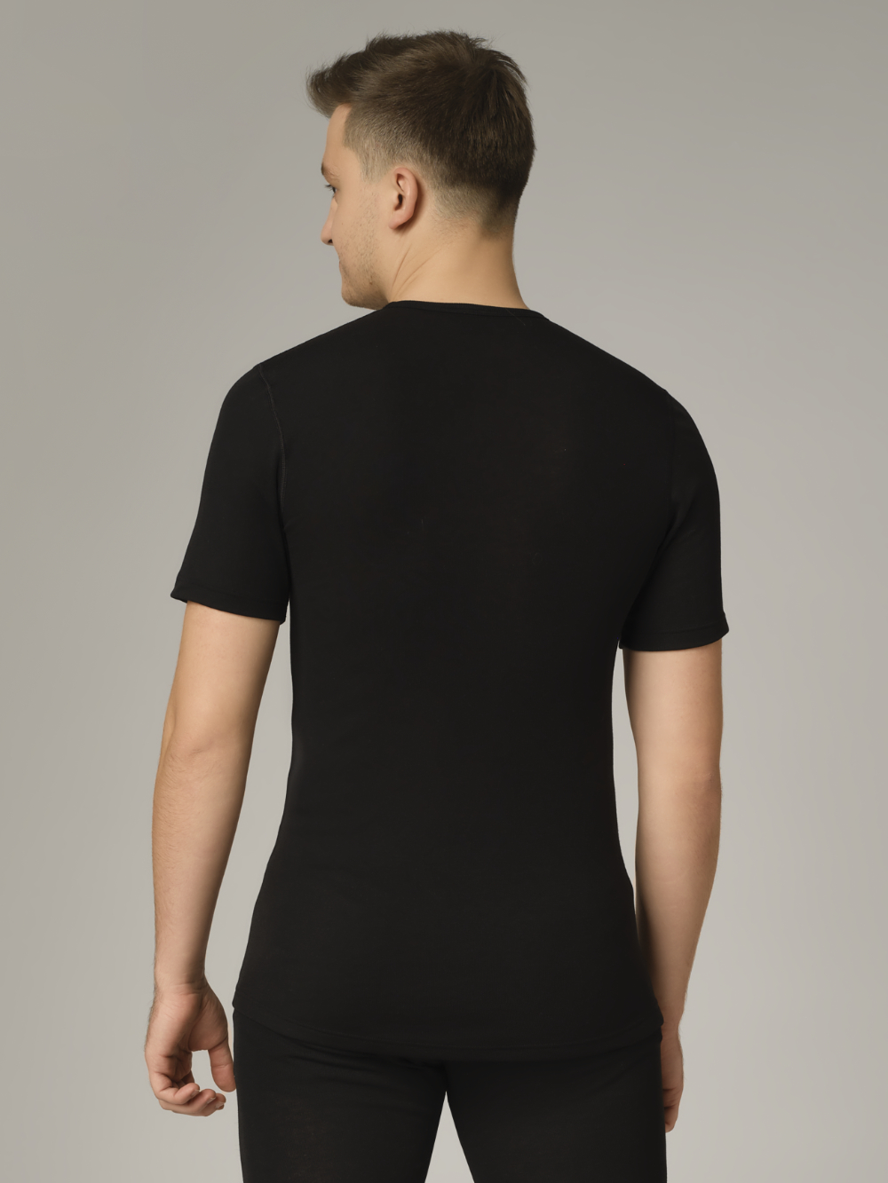 Comazo unisex short-sleeve functional shirt "warm extra", color black. Rear view: Man wearing unisex short-sleeve functional shirt "warm extra" by Comazo in black, with a brushed inner lining for optimal heat retention, moisture management, and an extended back panel.