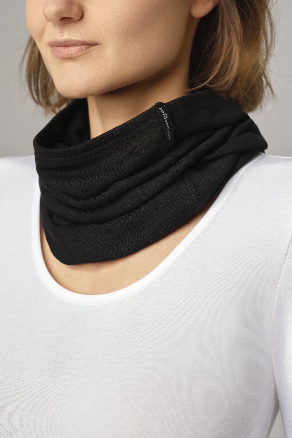 Comazo unisex scarf, color black. Front view: Woman wearing unisex scarf by Comazo in black, with a brushed inner lining for optimal heat retention and quick-drying functional fabric thanks to excellent moisture management.
